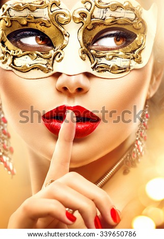 Beauty model woman wearing venetian masquerade carnival mask at party over holiday glowing gold background. Christmas and New Year celebration. Glamour lady with perfect make up and hairstyle