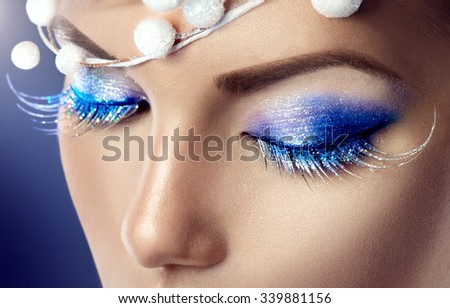 Winter Christmas eyes make up with glitter blue eyeshadows and false eyelashes. Party art model Woman makeup. Creative Girl Holiday Make-up. Snow Queen High Fashion Portrait over Blue Background