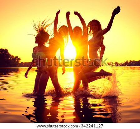 Vacation. Beach Party. Teenage girls having fun in water. Group of happy young people dancing at the beach on beautiful summer sunset. Silhouettes of group of teen girls jumping. Joyful friends