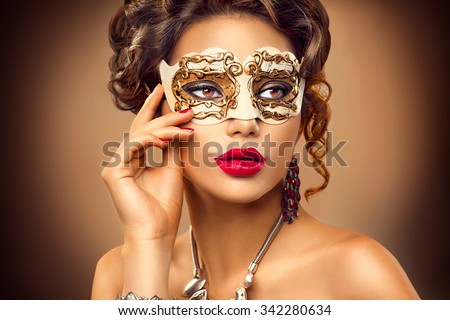 Beauty model woman wearing venetian masquerade carnival mask at party, over holiday background. Christmas and New Year celebration. Sexy girl with holiday makeup and manicure. Red lips and nails