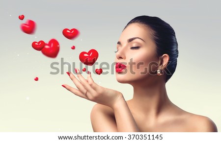 Beauty Woman with perfect make up Blowing Valentine hearts. Valentine\'s Day Beautiful Fashion sexy Girl showing copy space on the open hand. Gestures for advertisement