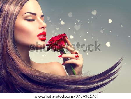 Beauty Fashion Model Woman with red rose flower. Red Lips and Nails. Valentine\'s Day Beautiful Fashion sexy Girl with flying long hair. Beautiful Sexy Brunette with Luxury Makeup and Manicure
