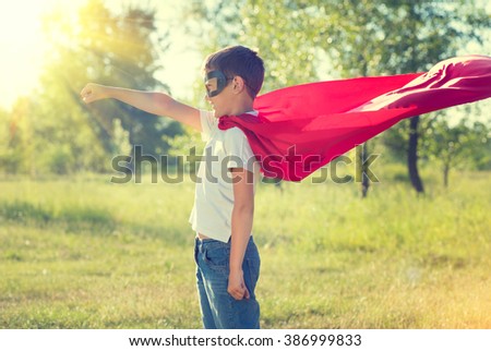 Super Hero Kid having fun outdoor. Superhero little boy over nature green blurred background. Little boy wearing superhero costume and having fun outdoors