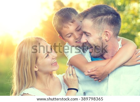 Happy young family having fun outdoors. Joyful young family father, mother and little son playing together in spring park. Mom, Dad and kid laughing and hugging, enjoying nature outside. Piggyback