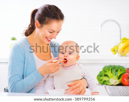 Mother Feeding Her Baby Girl with a Spoon. Mother Giving Food to her adorable Child at Home. Baby food