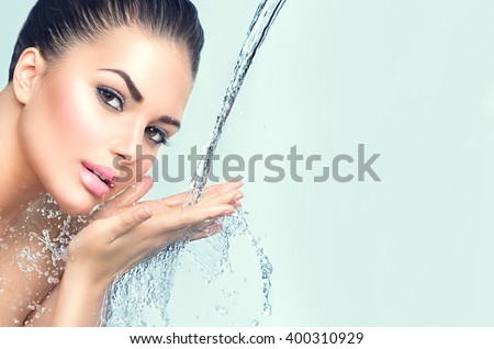 Beautiful Model Woman with splashes of water in her hands. Beautiful Smiling girl under splash of water with fresh skin over blue background. Skin care Cleansing and moisturizing concept. Beauty face