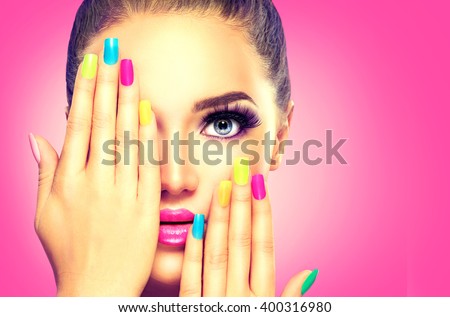 Beauty Girl Face with Colorful Nail polish. Colourful Studio Shot of young Woman. Vivid Colors. Colourful Manicure and fashion Makeup. Rainbow Colors. Beautiful lady touching her face