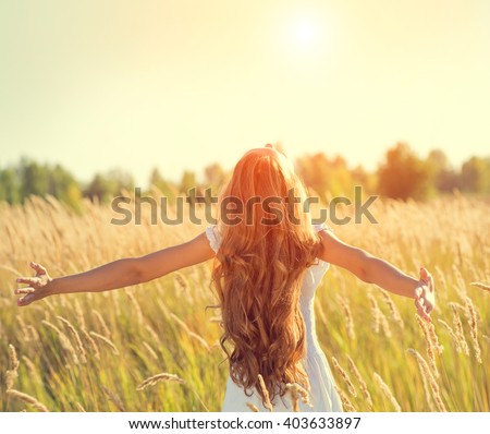 Beauty Girl Outdoors enjoying nature. Beautiful Teenage Model girl in white dress running on the Spring Field, Raising hands in Sun Light.