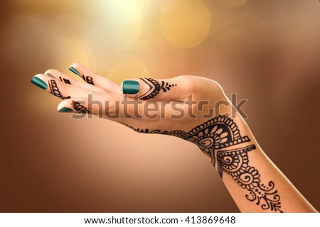Woman Hand with black mehndi tattoo. Hand of Indian bride girl with black henna tattoos. Showing empty copy space on the open hand. Proposing a product. Advertising gesture over brown blurred bokeh