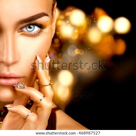 Beauty Fashion woman with Golden Makeup, gold accessories and nails. Girl Portrait with gold rings and manicure with crystals closeup isolated on black background. Fashion art make up