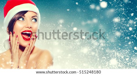Christmas sale. Beautiful surprised Woman in Santa Claus hat over Xmas Winter Holiday winter background with snow, Emotions. Funny Laughing Woman Portrait. New year sales