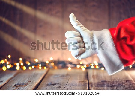 Santa Claus Thumb up gesture over Christmas holiday wooden background. Winter holiday table background decorated with Christmas garlands. Beautiful Empty Christmas room.
