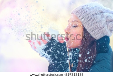 Winter girl blowing snow. Beauty Joyful Teenage Model Girl having fun in winter park. Beautiful young woman laughing outdoors. Enjoying nature.