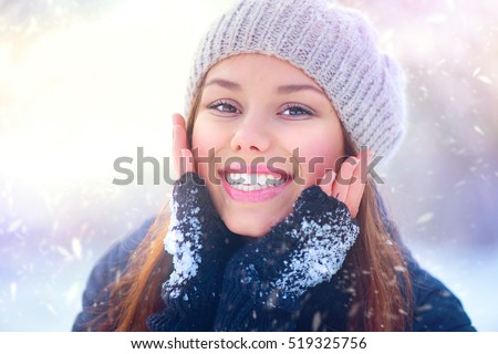Winter girl portrait. Beauty Joyful Teenage Model Girl touching her face skin and laughing, having fun in winter park. Beautiful young woman laughing outdoors. Enjoying nature.