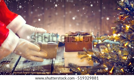 Santa Claus putting gifts under the Christmas tree with blinking garlands. Santa Claus giving gift box, holding a gift in his hands over wooden background.
