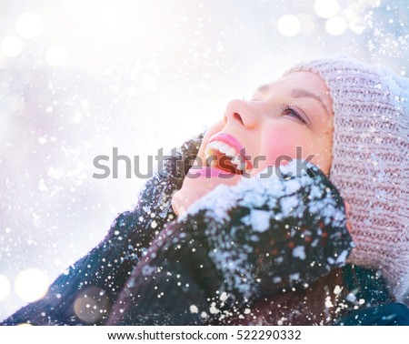 Winter girl portrait. Beauty Joyful Teenage Model Girl touching her face skin and laughing, having fun in winter park. Beautiful young woman laughing outdoors. Enjoying nature, wintertime