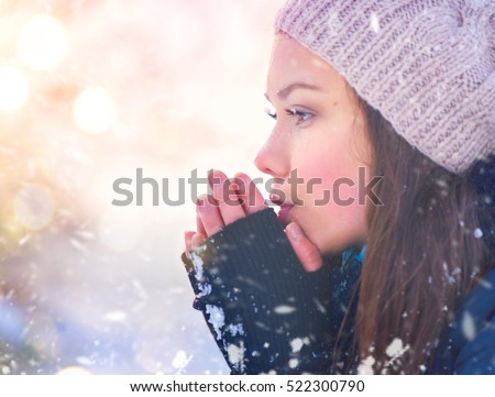 Winter girl blowing on her hands, cold weather. Snow. Frost, Freeze, Teenage Model Girl walking in winter park. Beautiful young woman outdoors. Cold weather concept, frozen hands