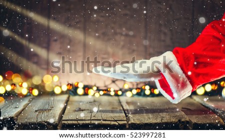 Christmas Santa Claus showing empty copy space on the open hand palm for text. Proposing product. Advertisement gesture presenting point. Holding gift, text or product over wooden background