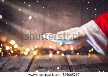 Christmas Santa Claus showing empty copy space on the open hand palm for text. Proposing product. Advertisement gesture presenting point. Holding gift, text or product over wooden background