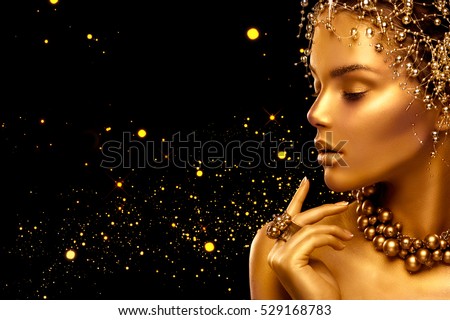 Gold Woman skin. Beauty fashion model girl with Golden make up, hair and jewellery on black background. Gold ring and necklace. Metallic, glance Fashion art portrait, Hairstyle and make up