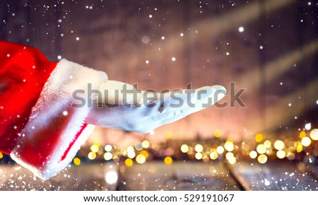 Christmas Santa Claus showing empty copy space on the open hand palm for text. Proposing product. Advertisement gesture presenting point. Holding gift, text or product over wooden background.
