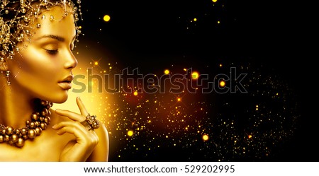 Gold Woman skin. Beauty fashion model girl with Golden make up, hair and jewellery on black background. Gold ring and necklace. Metallic, glance Fashion art portrait, Hairstyle and make up