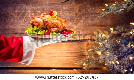 Christmas Holiday dinner. Santa Claus hand holding roasted Chicken. Christmas and New Year food concept, over rural wooden background