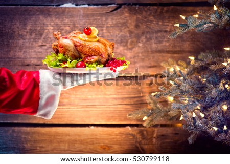 Christmas Holiday dinner. Santa Claus hand holding roasted Chicken. Christmas and New Year food concept, over rural wooden background and Decorated Christmas tree with lights