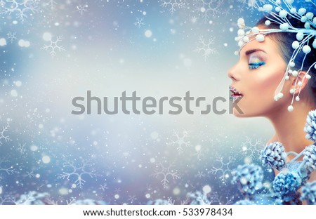 Winter Beauty Woman. Christmas Girl Makeup. Holiday Make-up. Snow Queen High Fashion Portrait over Blue Snow Background. Eyeshadows, False Eyelashes and Crystals on the Lips. Copy Space for Your Text