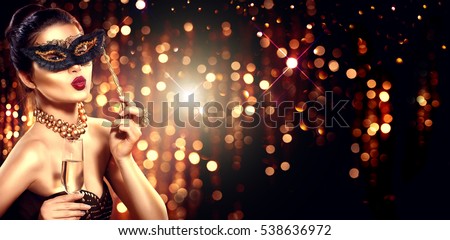 Beauty Glamour Woman celebrating with champagne, wearing carnival mask. party, drinking champagne over holiday glowing background. Christmas and New Year celebration.
