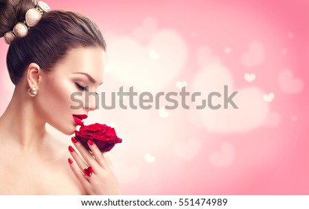 Beauty Valentine's Day Woman with red rose. Fashion Model Girl face profile Portrait with Red Rose in her hand. Red Lips and Nails. Pink blurred background. Beautiful Luxury Makeup and Manicure, hair.