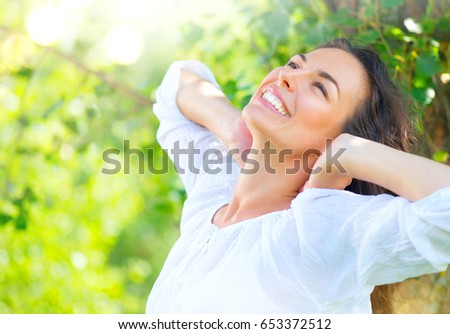 Beautiful Young Woman Enjoying nature Outdoor. Happy and Healthy Smiling brunette Girl with healthy smile relaxing in the Summer Park. Breathing fresh air. Sunny day. Health care concept