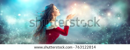 Christmas Winter Fashion Girl blowing  Magic snow in Her Hand. Fairy. Beautiful New Year and Xmas Tree. Holiday Hairstyle, Makeup. Gift. Beauty Model woman on Holiday Blurred blue Background, sale