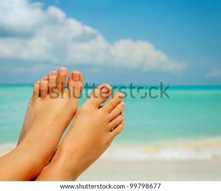 Vacation Concept. Tanning on the Beach. Woman\'s Bare Feet over Sea background