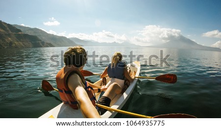 Outdoor Nature Selfie of Young Lovely Couple Canoeing Kayaking on Sunny Day on Lake Sea with Mountain View Background. Best Friends Enjoying and Having Fun Together on Kayak in Vacation Holiday Trip.