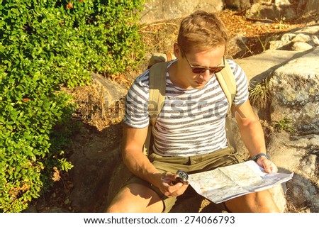 Handsome traveler man searching right direction on map - orange sunset light - sitting guy take a break after walking inside woods -  traveling along Europe, freedom and active lifestyle concept