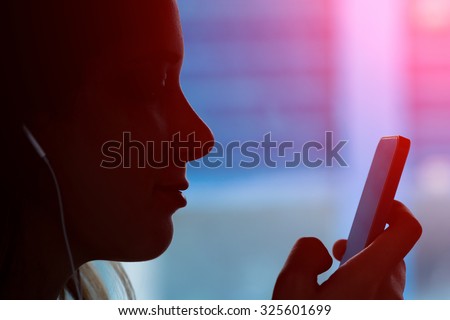 Silhouette of young girl with a phone sitting in the train and listening music - Face of a women typing a message on the smartphone during a travel - Main focus on the lips with marsala halo flare