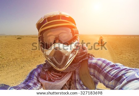 Happy young guy take selfie during desert excursion by quad - Man in helmet and adventure clothes make photo during vacation in exotic scenarios - Concept of activity holiday, freedom and adventure