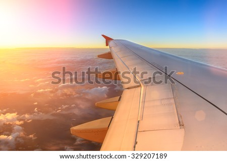 Aerial view of airplane flying above shade clouds and sky from an airplane fly during the sunset. View from the plane window of emotional moment during international travel around the world.