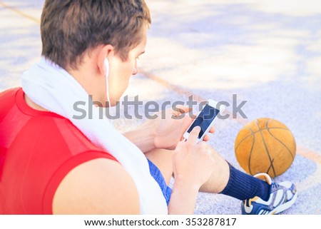 Sitting player in basketball court listen music with headphones after match with friends. Sport man collecting his thoughts before a game. Young guy finish do fitness session, jogging workout concept