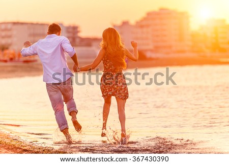 Rear view of happy couple running in summer on the beach in a tropical place. Two lovers in vacation in an idyllic nature scene sharing positive feelings and emotions. Magic moments  of loving hearts.