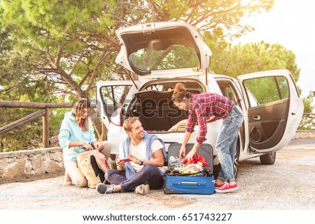 Happy young people pack their suitcase for a beautiful roadtrip holiday adventure with the car. Best friends chill and having fun making jokes about the travel trip. Concept af adventure and travel.