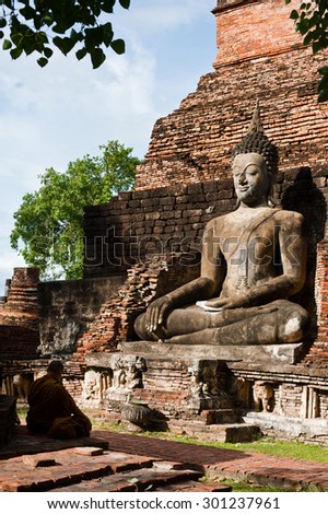 A monk meditating in front of buddhas statue large in SUKHOTHAI, THAILAND