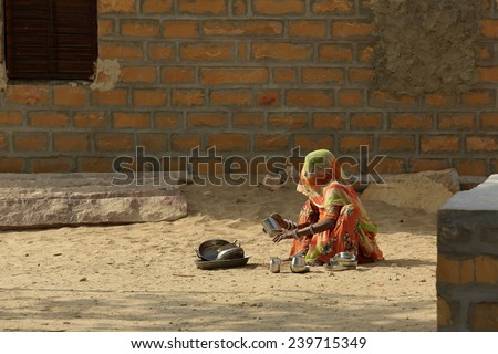 JAISALMER,INDIA - November 9,2014 : Unidentified indian woman dressed traditionally cleans the pots by using sands as a cleaner.