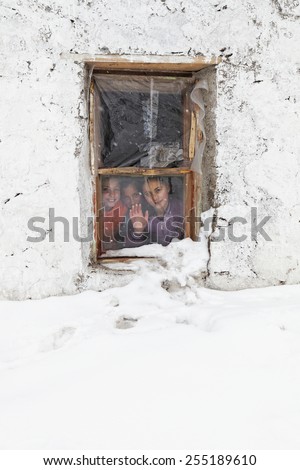 KARS,TURKEY - January 29,2013 : Unidentified children wave behind the broken and patchy window covered with snow in winter time in Kars,Turkey