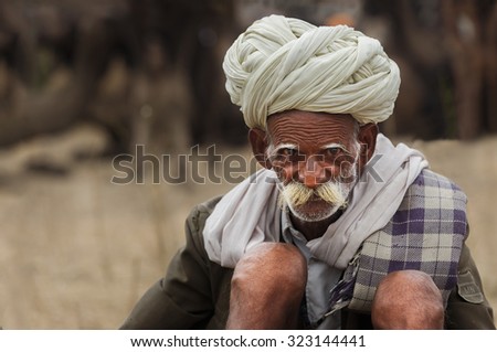 Pushkar, India - November 1, 2014 : Unidentified old Indian tribal man with his traditional dress and turban, sits on the sands of deseret in Pushkar Camel Fair,India
