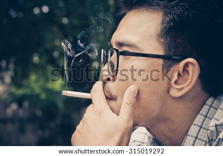 Closeup photo of man hold a smoking in outdoor and wearing a spectacles : The dangers of smoking : The source of lung disease : Vintage tone of man a smoking