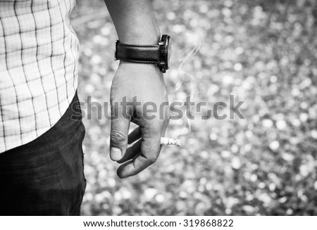 Closeup image of male hold a Cigarette in outdoor, black and white tone and wearing a black watch : the dangers of tobacco smoke, causes of lung disease.