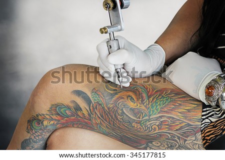 Girl tattoos artist showing processing of making a tattoo at leg. Tattoo design in pattern,bird swan tattoo. Tattoos art on human body skin colorful tone. Tattooist machine,gun.