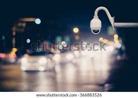 CCTV camera for surveillance driving operating on at night road. Abstract blur bokeh of car dark tones background.